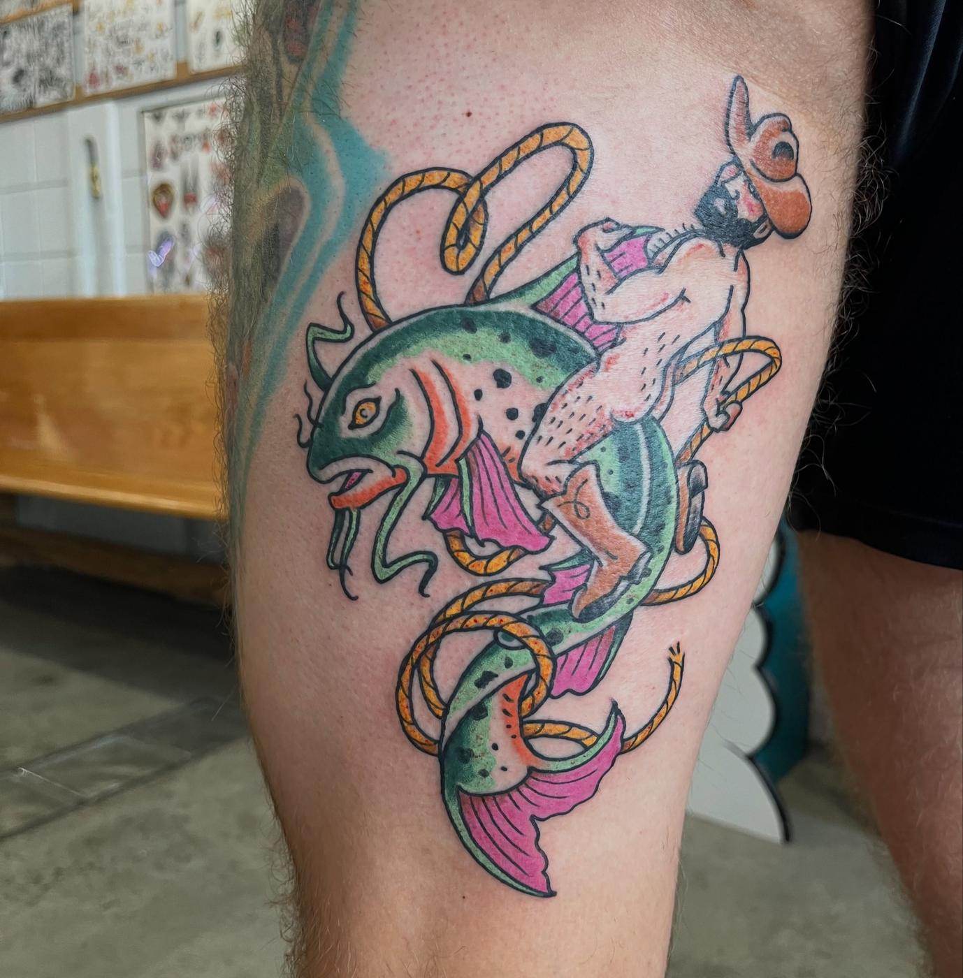 A color traditional tattoo of a rainbow trout wrapped in rope, on a thigh